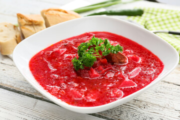 Bowl with tasty borscht on light wooden background, closeup