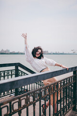 A happy girl on the river bank, standing on the bridge, smiling, a girl walks on the bridge by the river. Freedom. The wind is blowing the girl's hair.