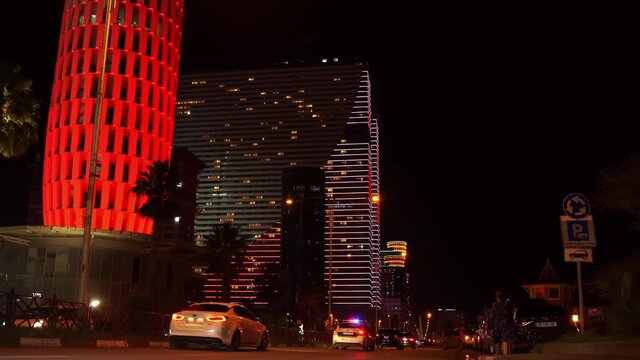 Night walk in Batumi. Colorful modern buildings of Orbi towers hotel illuminated by LEDs by the lake with dancing fountains show. Modern Georgian resort 