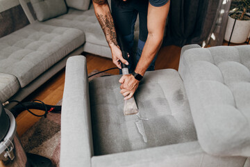 Handsome young man cleaning furniture. Process of deep furniture cleaning, removing dirt from sofa....