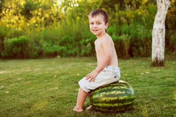 portrait of happy child boy with a large whole watermelon in the back yard