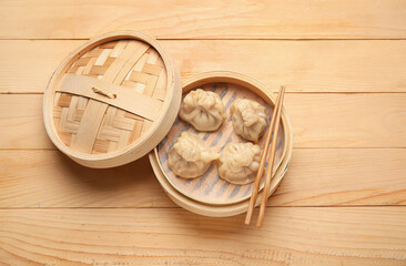 Bamboo steamer with tasty dumplings and chopsticks on wooden background