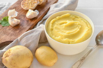 Bowl of tasty mashed potatoes with garlic and vegetables on white wooden background