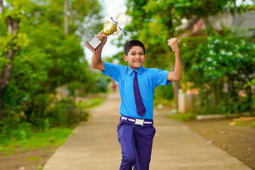 Clever schoolboy raising his trophy as a winner in school competition.