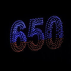 Colorful drone light shows on a night sky background. A figure of the number 650 made of glowing drones.