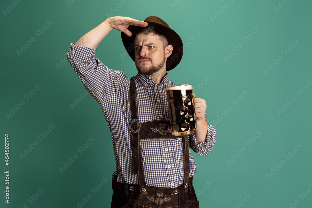 Wall mural Portrait of bearded man in traditional Bavarian costume with one liter of dark beer isolated over green background. Octoberfest, Festival concept