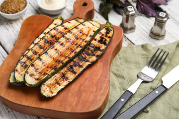 Board with tasty grilled zucchini on light wooden background