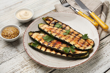 Plate with tasty grilled zucchini on light wooden background