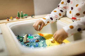 Montessori material. Children's hands play with sand and little toys. Kinetic sand in sandbox. Sensory development.