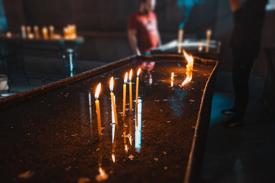 A lot of candles are burning in a medieval dark Catholic church and rays of light make their way through a narrow window. The concept of faith and religious feeling
