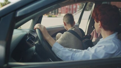 Handheld tracking shot of young mother with short red hair sitting in car and hugging her 13-year-old schoolboy before he leaves for first day of new school year