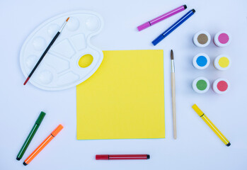 school supplies, pens, markers, paintbrushes, paints, palette with yellow paper mock up, free copy space