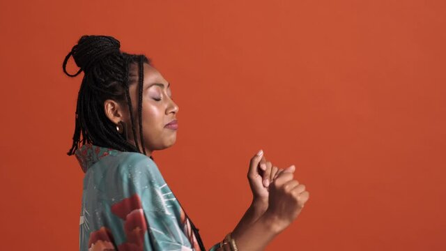 A side view of a relaxed african american woman dancing isolated over a red background in the studio