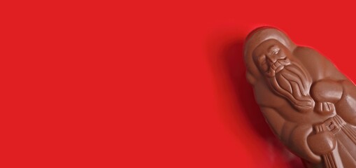 Delicious chocolate santa claus on red background. Panoramic image with copy space. 