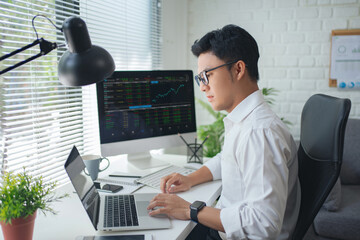 Concentrated young asian modern man in formalwear working using computers while sitting in the office
