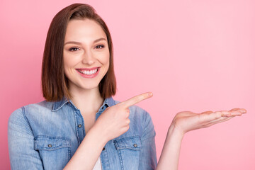 Photo portrait of girl keeping blank space on hand smiling pointing finger isolated pastel pink color background