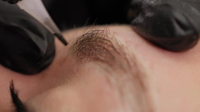 Close-up of a beautician doing permanent eyebrow makeup for a young woman in a beauty salon.
