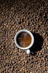 A cup of black coffee with milk is on top of roasted coffee beans.