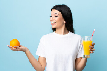 Young brunette girl over isolated blue background holding an orange and an orange juice