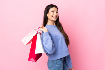 Fototapeta na wymiar Young brunette girl over isolated pink background holding shopping bags and smiling
