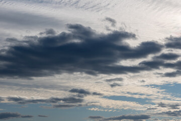 White-gray clouds in the sky illuminated by the setting sun. Light blue sky behind dark and dramatic storm clouds.