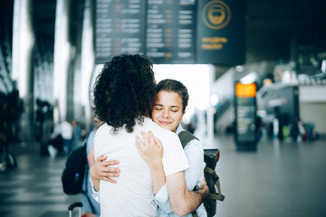 Young family couple at the airport departure area saying goodbye or hello, embracing each other...