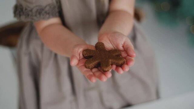 4k video of small hands of happy proud little baby girl making tasty Christmas sweets in holiday kitchen. Chid holding in hands raw gingerbread cookie in shape of snowflake showing it into camera