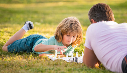 Fototapeta premium happy family of dad and son child playing chess on green grass in park outdoor, tactic
