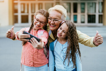 Happy grandmother came to pick up her grandchildren at school. They are taking selfie together.