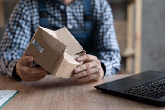 Close-up of male hands holding a crumpled box with goods near a laptop.