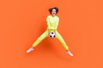 Fototapeta na wymiar Full length body size view of attractive cheery girl jumping playing soccer match isolated over bright orange color background