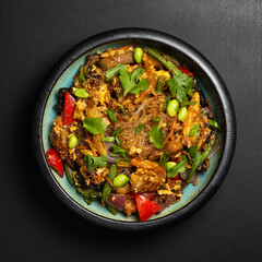 Udon stir-fry noodles bowl and vegetables on black stone background. Asian cuisine. Top view. Copy...