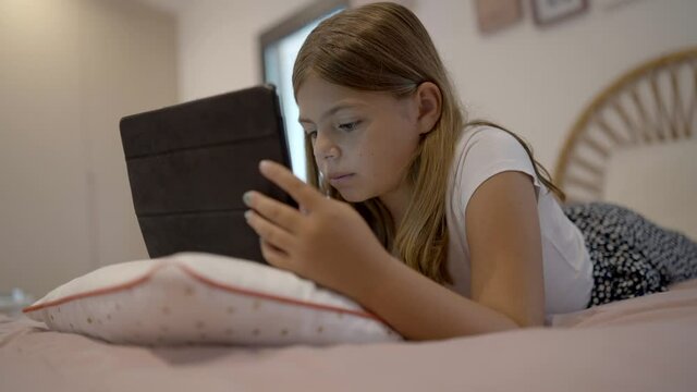 young girl with her tablet watching a video film in her bedroom