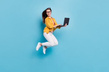 Full size photo of charming happy young woman jump up hold computer isolated on pastel blue color background