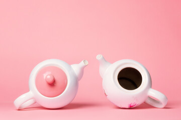 Breast Cancer Awareness Month. Two white porcelain teapots lying on a pink background. One teapot...
