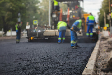 Process of asphalting, blacktopping and paving, group of workers with shovels finishing the asphalt layer, with asphalt paver machine and steam roller compactor vehicle in the background