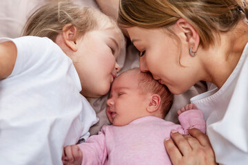 Mom and little daughter kiss a newborn baby in pink clothes. Happiness, love and tenderness. Close-up.