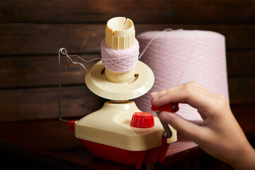 The girl rotates mechanical yarn winder or reel while rewinding thread. Close-up, selective focus - obrazy, fototapety, plakaty