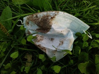 dirty and used disposable mask lying in the grass.