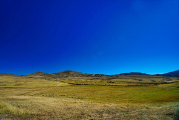 A dried out meadow in autumn. The background is blue sky and hills.