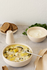 Chicken breast and sorrel soup with potatoes and sour cream, a bowl of soup on the table, bread and parsley