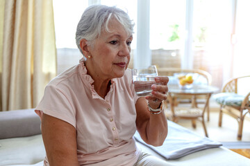 Cropped shot of a elderly woman drinking a glass of water at home. Senior woman with glass of water at home, age, healthcare and people concept. Shot of a healthy old lady holding a glass of water.