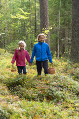 Fototapeta premium Two little girls carrying wicker baskets for gathering mushrooms and berries hiking in a forest in fall season, vertical