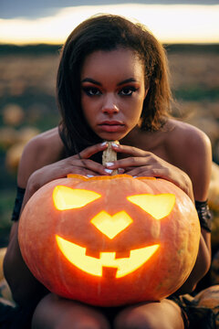Black woman holding big orange pumpkin with scary face in her hands. Halloween concept.
