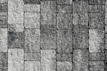 Concrete paving slabs with rounded corners and slightly uneven surfaces. The tile has a random uneven coloring and a coating of granite chips. View from above.