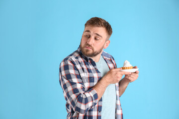 Greedy young man hiding cupcake on light blue background