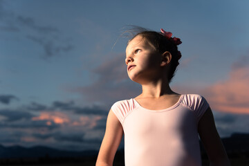 Dramatic outdoor portrait of a little ballerina girl at sunset. Child dreaming her future concept.