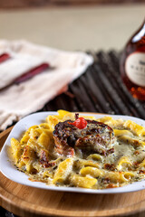 fettucine with white sauce, beef, beef medallion, mozzarella cheese and fresh basil on a white plate, red wine, black grill and rustic wall