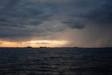 Sunset over the sea, with waves, stormy clouds and rain.