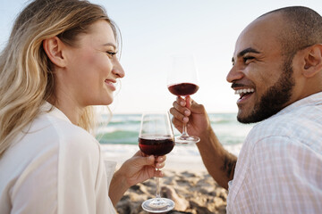 Portrait of a young couple sitting on the beach and drinking wine